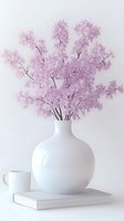 Delicate pink cherry blossoms in modern white ceramic vase on book with coffee cup, minimal spring composition against light background. Clean aesthetic styling.
