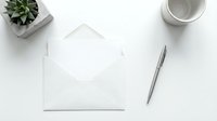 Minimalist white envelope with blank card on clean desk workspace with succulent plant, pen and coffee cup for correspondence and stationery design.