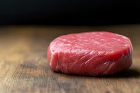 Raw beef tenderloin steak with marbled texture on rustic wooden surface, fresh premium cut meat ready for cooking, dramatic lighting and soft focus.