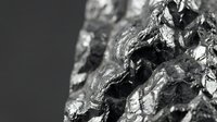 Raw silver ore mineral specimen with metallic luster and crystalline structure on dark background for geology education and mining industry materials.