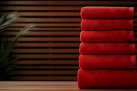 Stack of soft red folded towels on wooden surface with blurred striped background and green plant, spa and hotel linen concept.