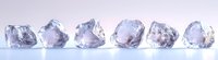 Raw uncut diamonds arranged in a row on light background, showcasing natural crystal formations with varying clarity and color for jewelry design or gemology study.
