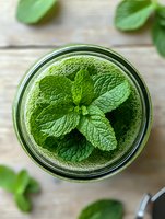 Fresh green smoothie with mint leaves in glass jar on wooden background for healthy lifestyle and detox diet concepts.