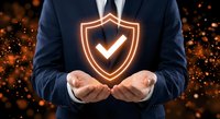 Professional businessman in suit holding glowing orange shield with checkmark symbol representing security, protection and trust in digital business environment.