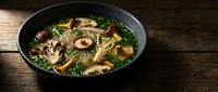Asian mushroom noodle soup with fresh herbs in black bowl on rustic wooden table. Hot broth with shiitake mushrooms and greens for restaurant menu design.
