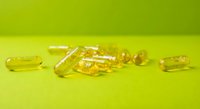 Yellow omega-3 fish oil capsules scattered on bright green surface for health and wellness supplement photography and marketing materials.