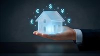 Businessman holding glowing holographic house with floating currency symbols, representing global real estate investment and property finance concepts.