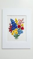 Colorful embroidered flower bouquet featuring blue delphiniums, red tulips, yellow daisies, and pink blossoms on cream linen fabric, mounted on white mat board for home decor and craft projects.
