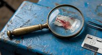 Vintage magnifying glass examining old postage stamp on weathered blue surface with ruler for philatelic collection study and historical postal research analysis.