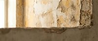 Weathered concrete wall with peeling paint and exposed layers showing age and deterioration in abandoned building interior for renovation projects.