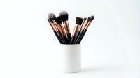 Professional makeup brushes with rose gold ferrules in white ceramic holder on clean background for beauty and cosmetics applications.