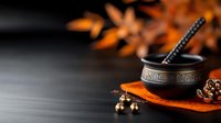 Tibetan singing bowl with striker on orange cloth surrounded by warm candlelight creating peaceful meditation atmosphere for wellness and spiritual practices.