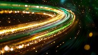 Glowing curved light trails in green and gold colors create dynamic motion effect against dark background with sparkle bokeh elements. Abstract night photography.