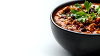 Spicy chili con carne with minced beef, kidney beans and fresh herbs served in black ceramic bowl on white background. Traditional Mexican cuisine.
