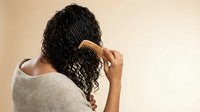 Young African American woman with curly hair using wooden comb for natural hair care routine and styling in bathroom setting for beauty and wellness.