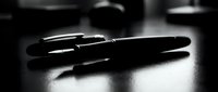Two black ballpoint pens arranged on reflective surface with dramatic lighting and shadows, suitable for business, writing, stationery, and office design projects.