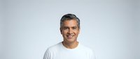 Smiling middle-aged Latino man with gray hair wearing a white t-shirt, isolated on a light gray background, exuding confidence.