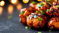 Glazed chicken meatballs garnished with fresh herbs on dark background with bokeh lights, close up view showing caramelized sauce and appetizing texture.