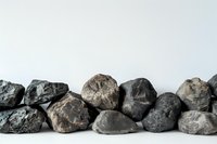 Row of natural rough gray and black stones arranged on white background, minimalist composition showing texture and mineral variety for design projects.