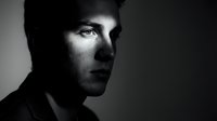 Dramatic black and white portrait of young Caucasian man with intense gaze and shadow lighting for professional headshots and artistic photography.