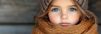 Young Caucasian girl with blue eyes wearing knitted winter hat and orange scarf looking at camera with serious expression during cold season outdoors.