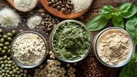 Organic superfood powder supplements in bowls with raw ingredients. Green spirulina, plant protein, and nutritional powders with fresh basil leaves on dark background.