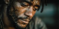 Close-up portrait of contemplative African American man with weathered face and intense expression showing resilience and determination in dramatic lighting.