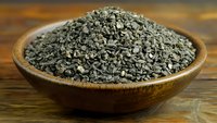 Crushed dark gray stones in wooden bowl on rustic table, natural mineral supplement or alternative medicine ingredient for wellness and health.
