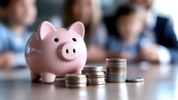 Pink ceramic piggy bank with stacks of coins arranged in ascending order on wooden table, business meeting background showing financial growth and savings concept.