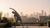Young athletic woman practicing yoga side bend pose on urban rooftop terrace at sunrise with city skyline backdrop for wellness and fitness lifestyle.