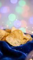 Golden crispy potato chips in blue bowl with colorful bokeh lights background for party snacks and celebration food concepts.