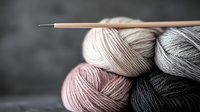 Soft wool yarn balls in pastel pink, beige and gray shades with wooden knitting needle on dark background, selective focus creates cozy crafting atmosphere.