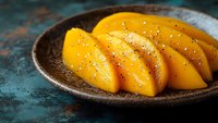 Fresh sliced mango with chia seeds served on rustic ceramic plate against teal textured background, perfect for food blog or recipe website.