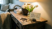 Rustic wooden console table with white tulips, vintage keys, and a welcome to your new home card, warm lamp light, cozy interior.