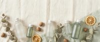 Natural skincare cosmetic bottles with eucalyptus leaves and dried orange slices on neutral background for organic beauty product mockup.