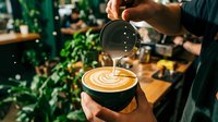 Professional barista creating latte art in coffee shop, pouring steamed milk into espresso cup with heart pattern design for cafe service and specialty beverage preparation.