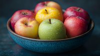 Fresh colorful apples with water drops in turquoise ceramic bowl on dark background, healthy organic fruits for natural food photography.