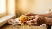 Mature male hands holding golden honeycomb with dripping honey, showcasing natural sweetener and apiary products for food, wellness, and culinary content.