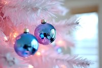 Pink and blue Christmas ornaments hanging on white artificial tree with warm lights creating festive holiday decoration atmosphere.