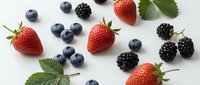 Fresh mixed berries including strawberries, blueberries and blackberries with green leaves scattered on white background for healthy eating concepts.