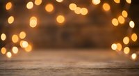 Warm golden bokeh lights create magical atmosphere over rustic wooden table surface for holiday celebrations and festive decorations.