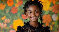 Young African American woman with braids and bright smile wearing black lace dress against colorful orange and yellow floral background, natural outdoor portrait.