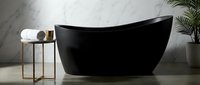 Sleek black freestanding bathtub in modern bathroom with marble walls, gold accent table, rolled towels, and potted plant for luxury spa design.