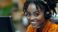 Young African American woman customer service representative wearing headset smiling at camera in modern office environment for business communications.