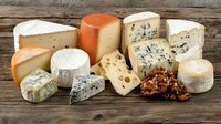 Gourmet cheese assortment with blue cheese, brie, gouda, and walnuts arranged on rustic wooden board. Variety of aged and fresh dairy products for fine dining.