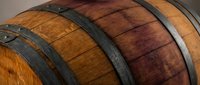 Wooden wine barrels with metal hoops stacked in cellar for aging spirits and beverages in winery or distillery storage facility.