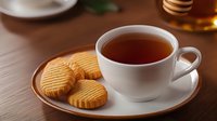 Steaming cup of black tea served with crispy butter cookies on white porcelain plate against wooden table background, cozy afternoon tea setting.