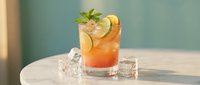 Refreshing orange cocktail with mint garnish and ice cubes on white table against soft blue background for summer beverage photography and bar menu designs.