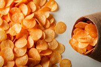 Fresh sliced carrots scattered on light surface with portion in rustic paper cone, overhead view of bright orange organic vegetable pieces for cooking.