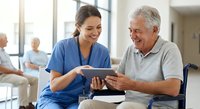 Smiling female nurse in blue scrubs showing tablet to happy senior male patient in modern healthcare facility waiting area with natural lighting.